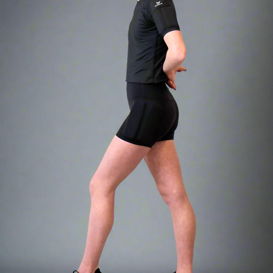 Girl standing showing her side of the body, wearing the black weighted short sleeves with weights on the arms and weights on the side of the leg, with the weights on the hip
