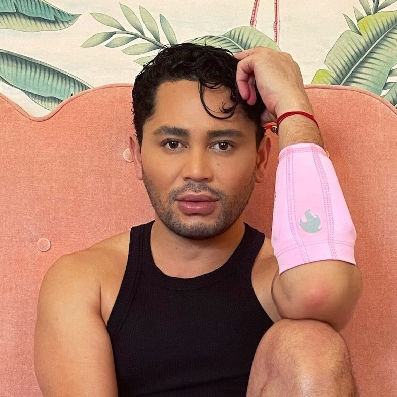 Image showing Isaac Boots sitting with a bent knee and his elbow resting on the knee, wearing the pink kilogear cut arm bands with the torch logo in silver and weights in the arm band