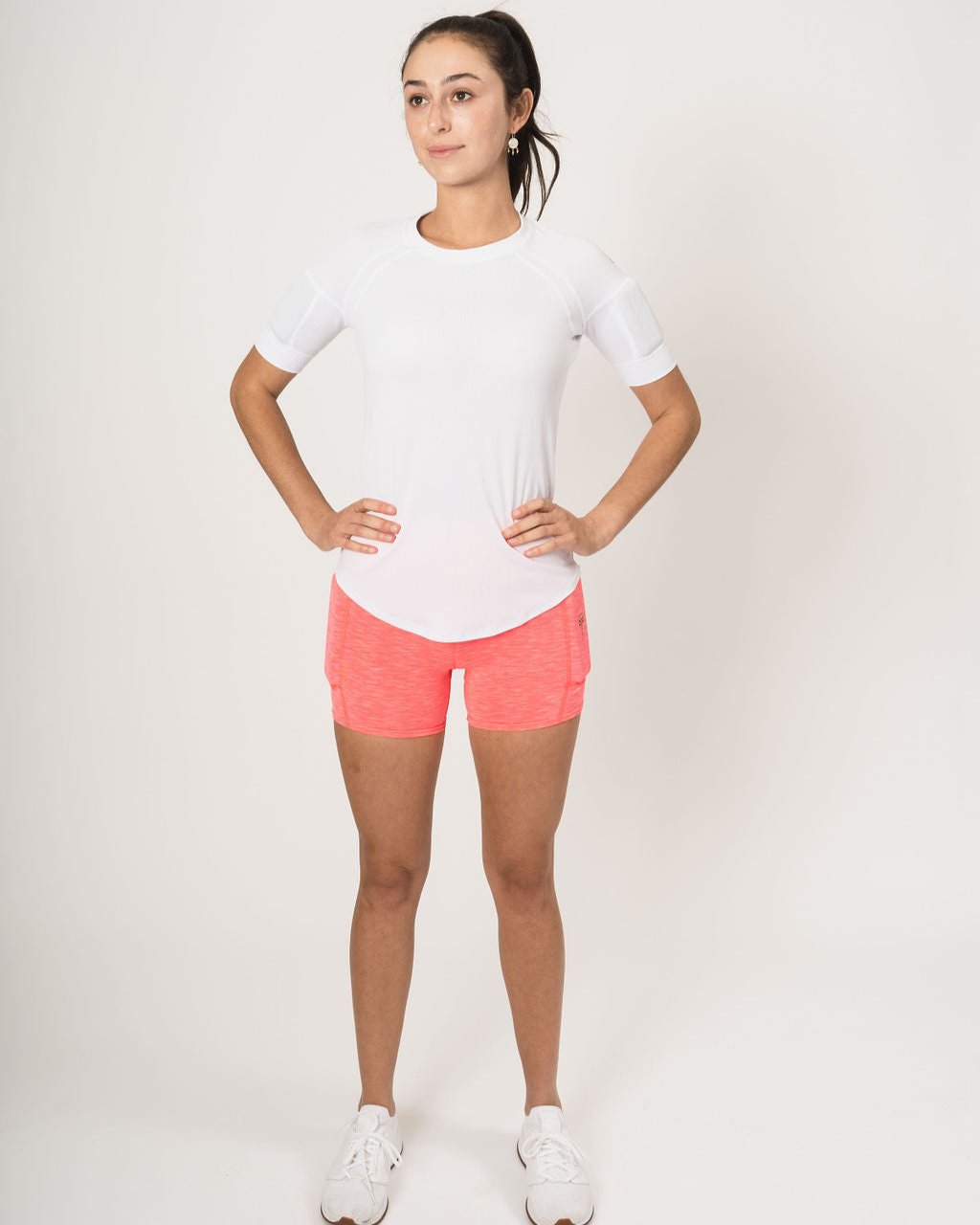 front picture showing woman wearing the weighted white short sleeve with weights on the biceps and the heather coral shorts with weights in the side weight pockets, found on the quads.