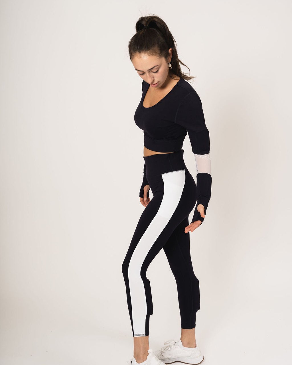 Model wearing the long sleeve scoop neck weighted shrug in navy with white accents and the weighted navy with white strip down the leg booty lift legging with weights on the calves.
