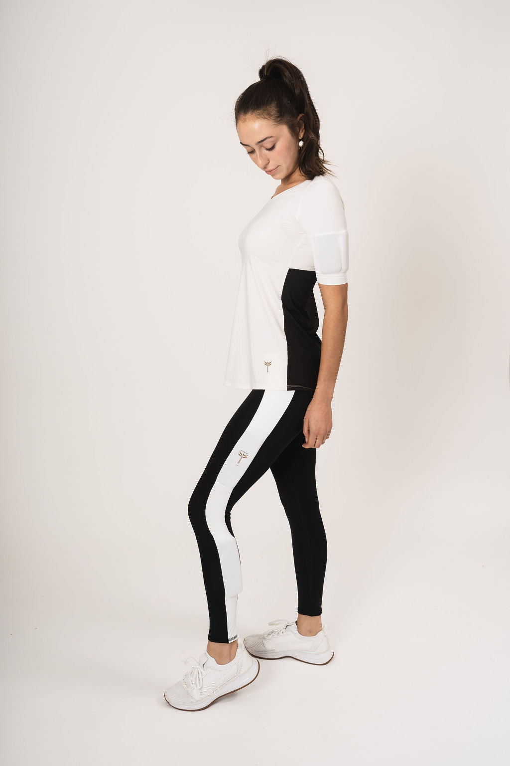 Side view woman wearing the relaxed fit weighted short sleeve. Top is all white in the front with  a scoop neck. The back has white at  the top and black mesh halfway down the back. Weights are in the bicep arm pockets. She is wearing the black booty lift legging with the white stripe down the side of the leg.