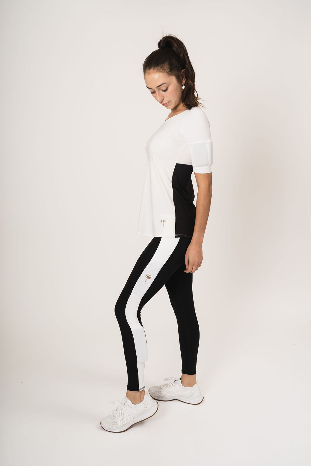 Side view woman wearing the relaxed fit weighted short sleeve. Top is all white in the front with a scoop neck. The back has white at the top and black mesh halfway down the back. Weights are in the bicep arm pockets. She is wearing the black booty lift legging with the white stripe down the side of the leg.