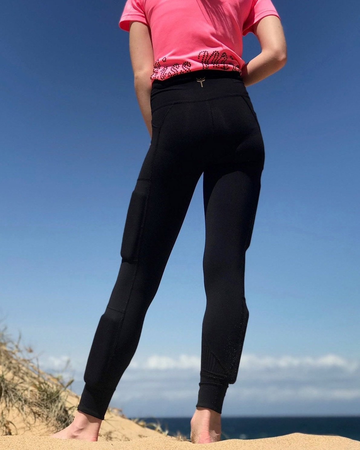 Rear view of the black legging with the kilogear cut logo on the back of the high waistband, weights on the side of the leg with one above the knee on the side and one below the knee on the side calf.