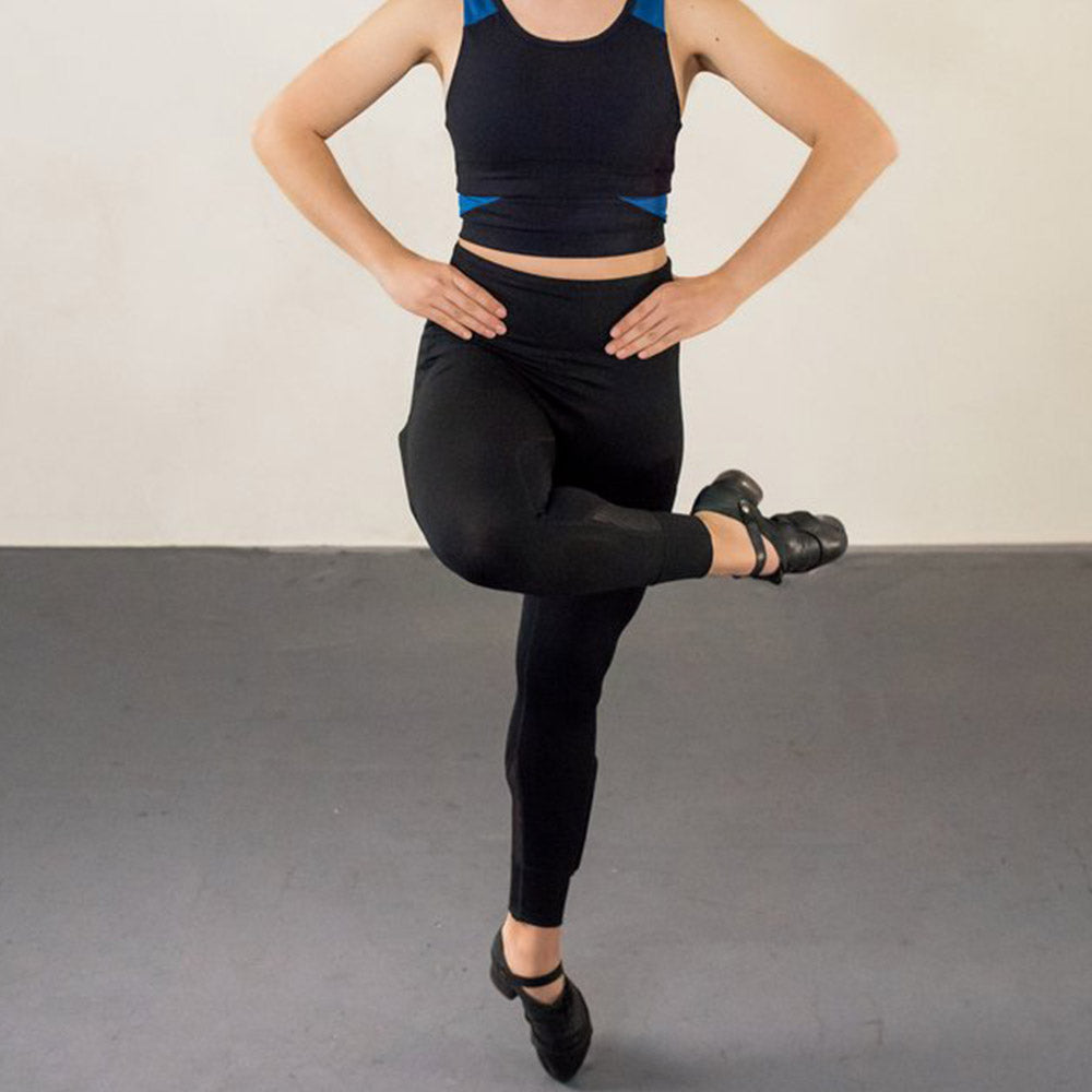 Woman dancing in black sports bra and black leggings dancing with her leg bent over the knee