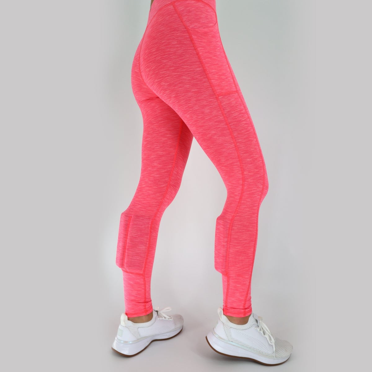 rear view. Woman wearing the heather coral weighted booty lift legging. Hand on the hip. The weights in the booty lift legging are found on the back side of the calves.