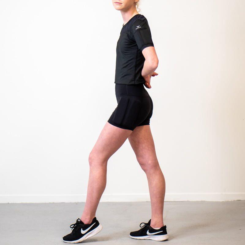 Girl standing showing her side of the body, wearing the black weighted short sleeves with weights on the arms and weights on the side of the leg, with the weights on the hip