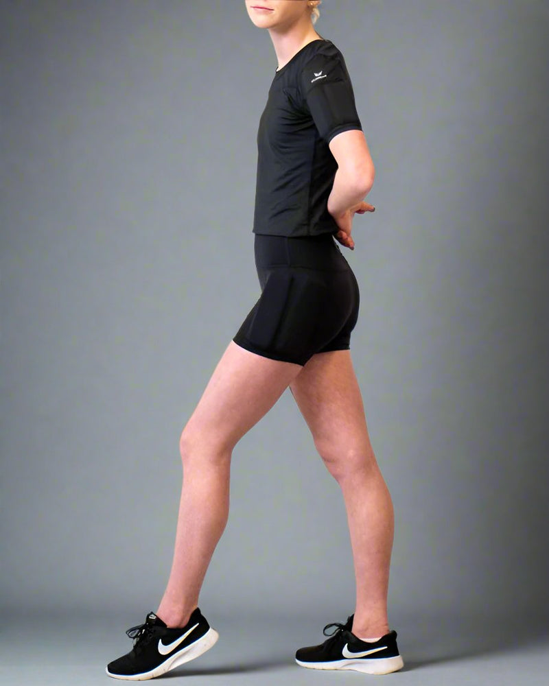 Girl standing showing her side of the body, wearing the black weighted short sleeves with weights on the arms and weights on the side of the leg, with the weights on the hip