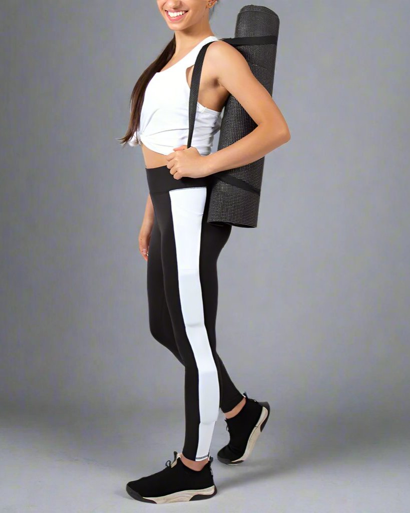 girl holding yoga mat wearing black kilogear cut legging with white strip down the leg, showing weight in the calf weight pocket and quad weight pocket, side view