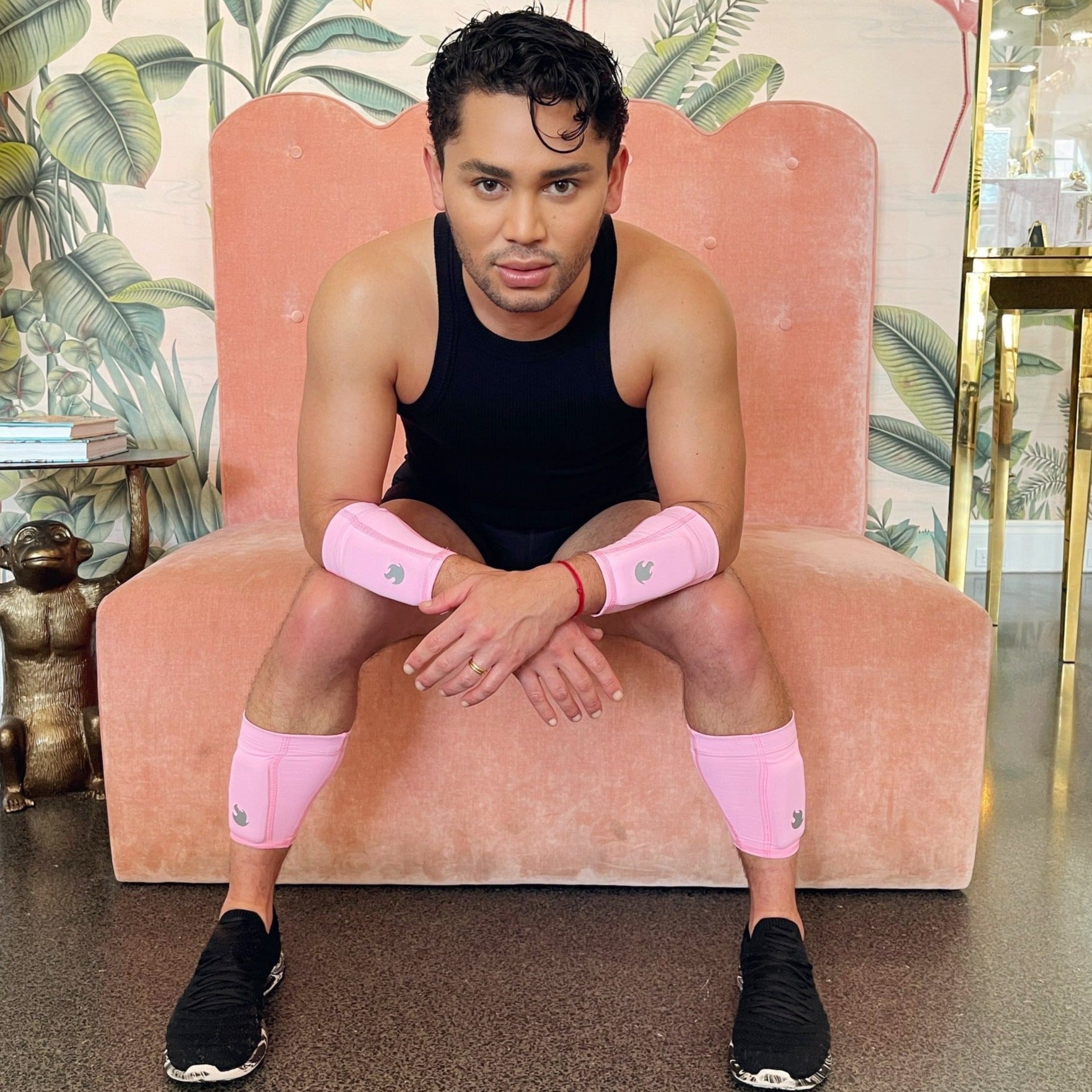 Image showing Isaac Boots sitting in a chair, leaning on his knees wearing the pink weighted arm and leg bands with the flame logo in silver on each band.