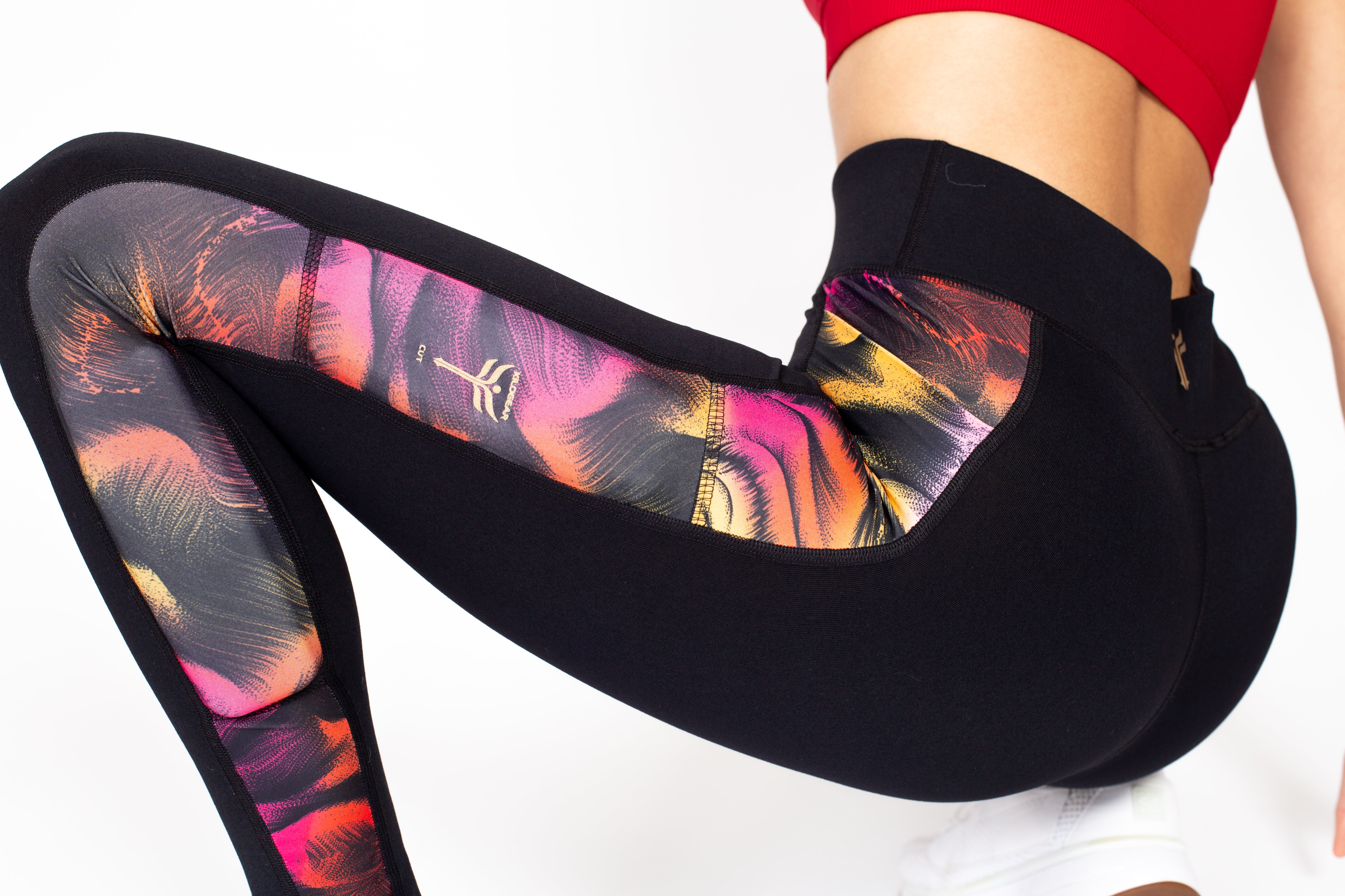 up close picture with woman crouched down and knees bent, wearing black kilogear cut legging with colorful strip down the leg, called passion fruit. Reds, yellows, pink and orange swirls.Showing weight in the calf weight pocket and quad weight pocket, side view