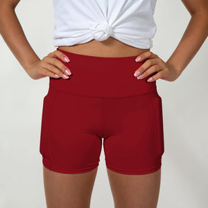 Front view of the maroon shiny short with hands on the hip and weights on the side of the leg, below the hip