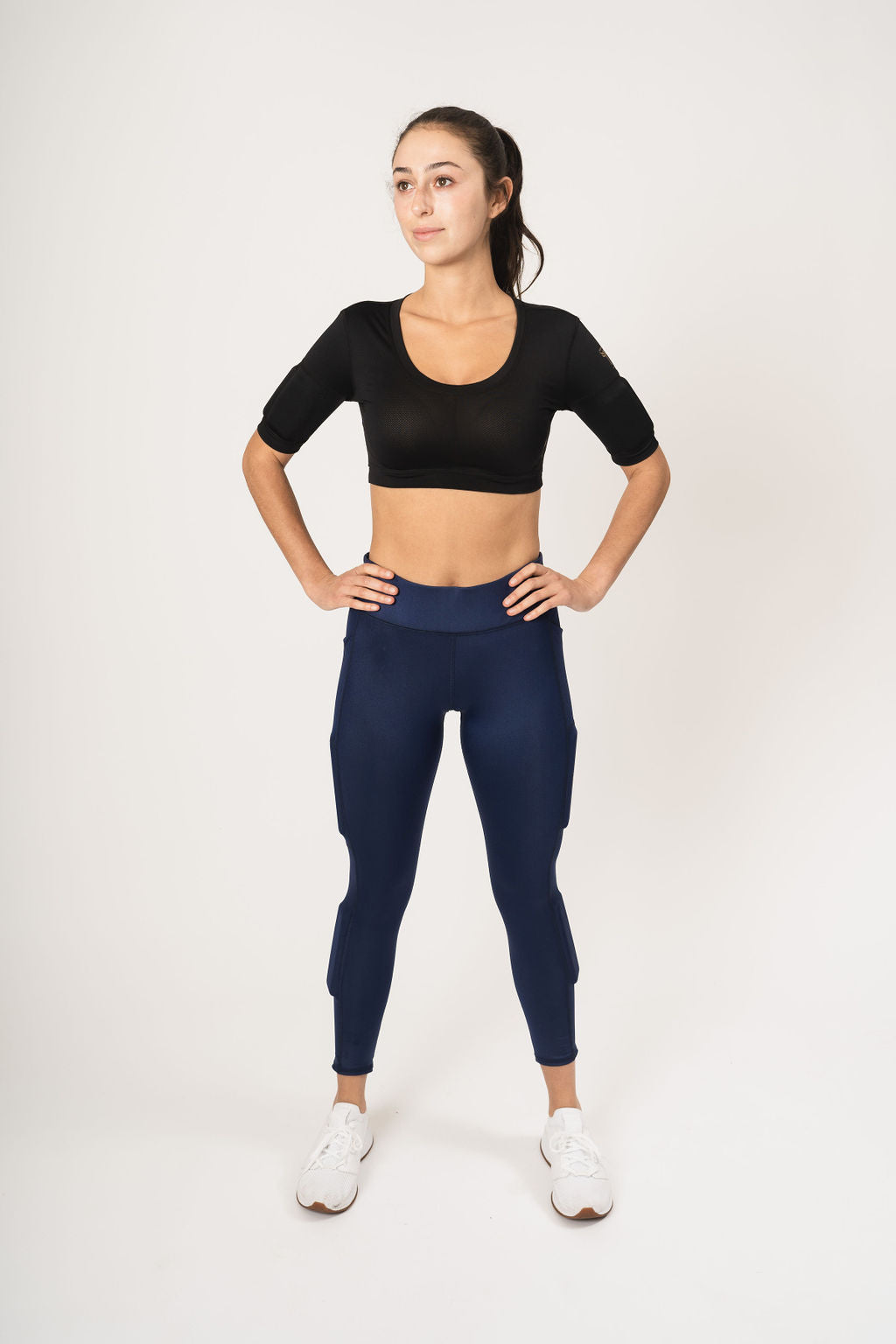 Woman standing with her hands on her hip wearing black weighted crop top and navy weighted leggings
