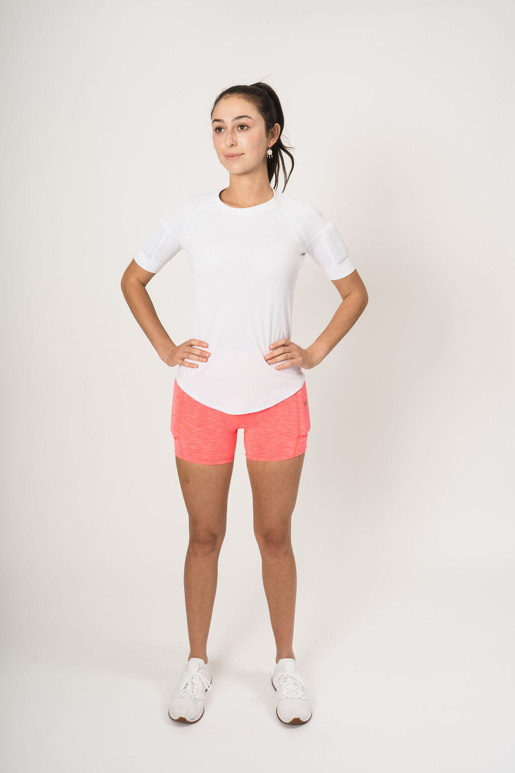 front picture showing woman wearing the weighted white short sleeve with weights on the biceps and the heather coral shorts with weights in the side weight pockets, found on the quads.