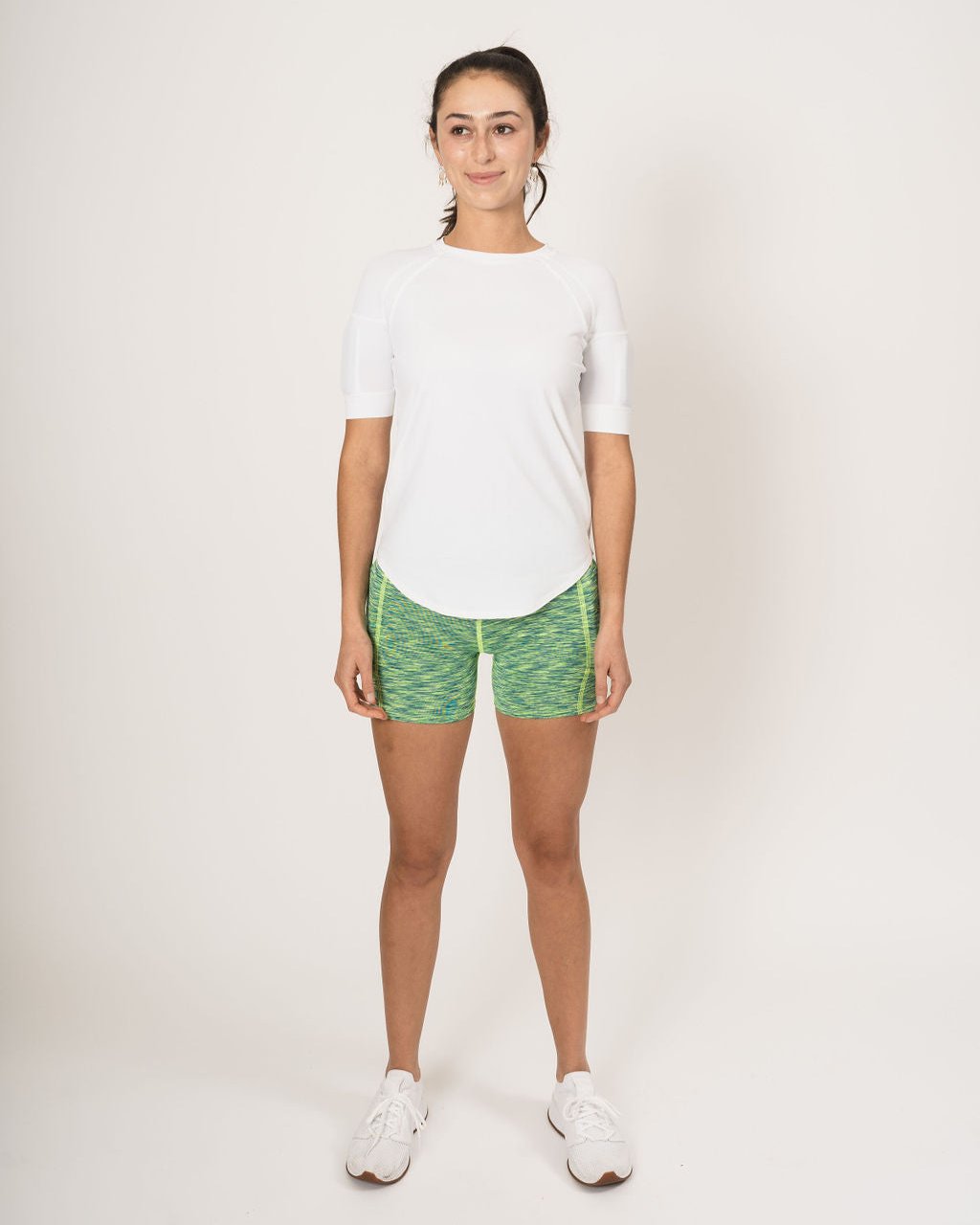 front picture showing woman wearing the weighted white short sleeve with weights on the biceps and the heather lime green shorts with weights in the side weight pockets, found on the quads.